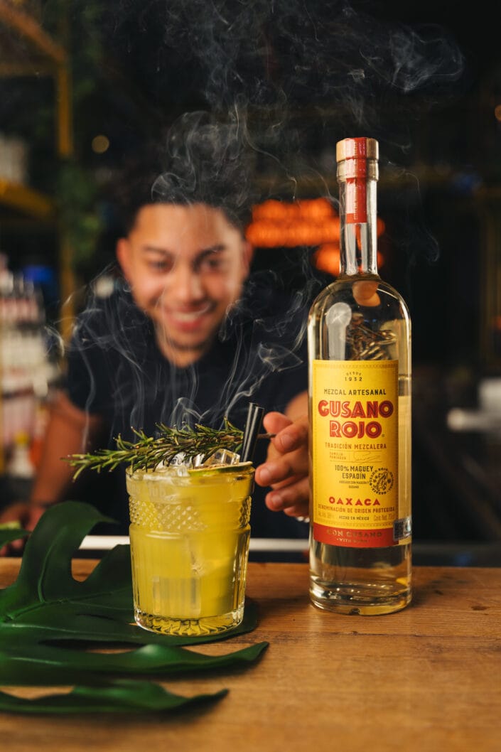 Bartender legt gebrande rozemarijn bovenop cocktail bij Tranquilo